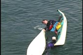 paddler in cockpit uses bow of overturned kayak to roll up